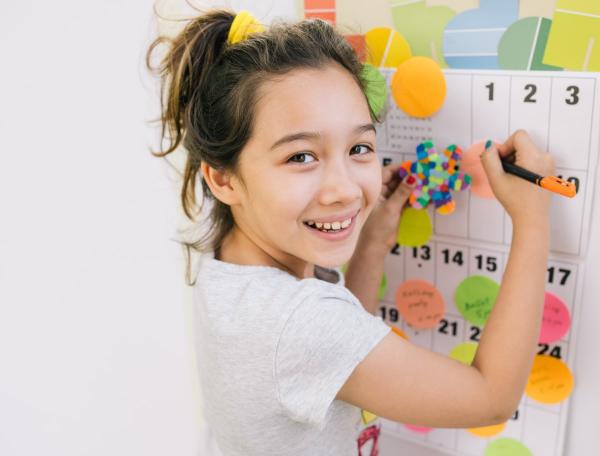 Girl using coloured circle sticky notes to mark a calendar 