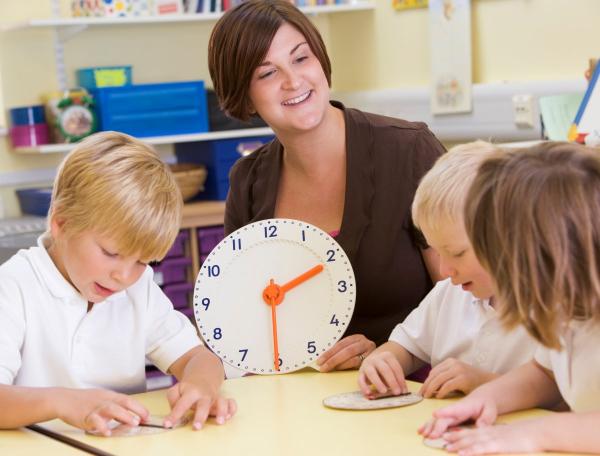 Children playing with hands on paper clocks learning to tell the time