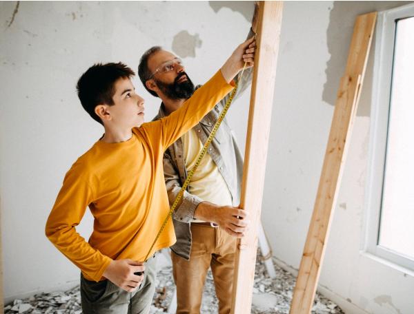 Father and son use a measuring tape to measure a wood paling 